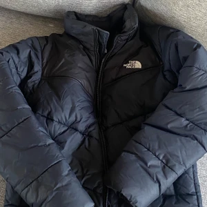 Svart dunjacka från The North Face - Snygg och varm svart dunjacka från The North Face med dragkedja och hög krage. Perfekt för kyliga dagar. 