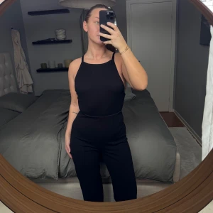 Svart ärmlös body - Snygg svart ärmlös body med smala axelband och öppen rygg. Perfekt för en stilren look. Tillverkad i ett stretchigt material som ger en tight passform och ribbat material. Normal i storleken 