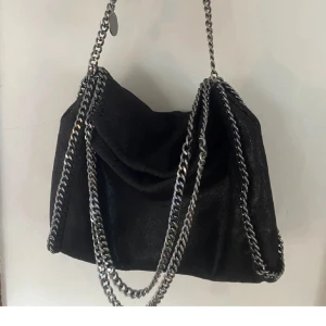 Svart axelväska med kedjedetaljer - Snygg svart axelväska med stiliga kedjedetaljer. Perfekt för att ge en edgy touch till din outfit. Väskan har en elegant design och är lätt att matcha med olika stilar.