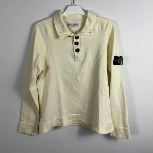 Beige långärmad pikétröja från Stone Island - Säljer en stilren beige långärmad pikétröja från Stone Island. Tröjan har en klassisk krage med tre knappar och det ikoniska märket på ärmen. Tillverkad i en mjuk bomullsblandning för extra komfort. Köpt från en vintage sida så den har några år på nacken.