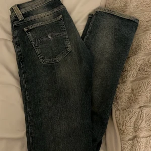 Blå jeans från Nudie Jeans - Snygga blå jeans från Nudie Jeans med klassisk femficksdesign och subtila slitningar. Perfekta för en avslappnad stil med en touch av edge. Märkeslogga på bakfickan och knappstängning fram.