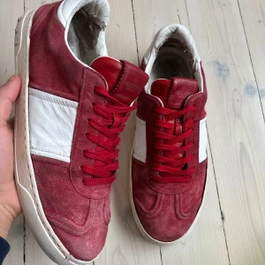 valentino flycrew Röda och vita  - Snygga röda sneakers från Valentino med vita detaljer och snörning. Skorna har en mockayta och en unik sula med mönster. Perfekta för en stilren look.kom gärna med bud priset är absolut inte hugget i sten!