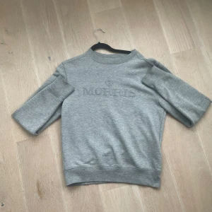 Grå sweatshirt från Morris - Säljer en stilren grå sweatshirt från Morris med diskret logga på bröstet. Tröjan har en klassisk rund hals och ribbade muddar vid ärmslut och nederkant. Perfekt för en avslappnad stil.