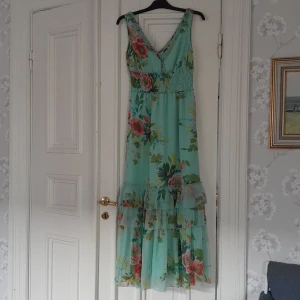 Sommarklänning - En härlig långklänning i blommigt turkost. En sval och somrig modell. Ryggen är likadan som framstycket. Midjan på klänningen är 68cm. 100% polyester. Tvättas 30° 