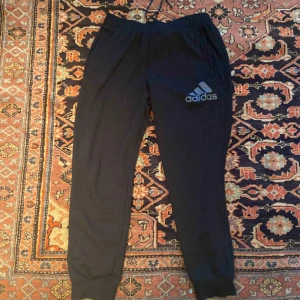 Adidas Sweatpants - Snygga svarta träningsbyxor från Adidas. Har blixtlåsfickor med 2 snören för att justera storleken. Har inte använt dem många gånger kanske runt 3 gånger. Skick 9/10.  meddelande mig om priset :)