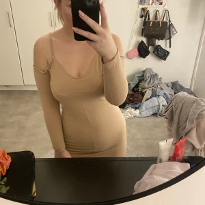 Klänning - Beige klänning med band och öppna axlar. Säkert mycket snyggare när man blivit lite brun och perfekt till sommaren. Den går ner till lite över knäna. Från hm.