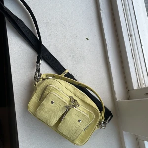 Liten väska från núnoo - Fin gul väska, bandet kan man reglera. Väldigt fint skick 