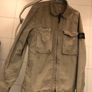 Stone island overshirt Beige - En Stone Island overshirt jag haft i ett par år, inköpt på Jupiter Norrlandsgatan. Aldrig kemtvättad eller tvättad alls.  Just den här modellen finns ej längre med två raka bröstfickor i butik.   Storlek M  Pris - 2100