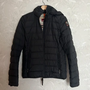 PARAJUMPER - Säljer min pjs jacka pga för liten i stoleken, den har bara ståt i garderoben och inte används. Modell: Juliet Hooded Down Jacket W Black • DWR-behandlat yttermaterial • Tvåvägsdragkedja • Fickor med dragkedja •Innerficka Ribbad innerkrage Justerbar huva 