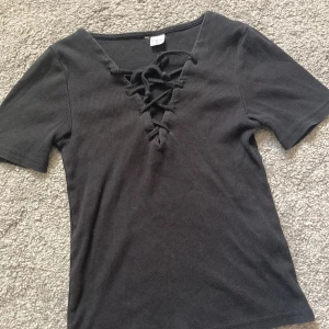 T-shirt med snörning, stl xs  - Svart ribbad t-shirt med snörning över brösten, använd ganska mycket men är inte i dåligt skick :)