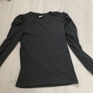 Topp med puffärmar  - En supersöt mörkgrå tröja med scrunchade axlar som superfin detalj. Tröjan är använd men i väldigt fint skick. Säljer då den är lite kort i armarna för mig har långa armar. Är en M men passar S. Pris kan att diskuteras