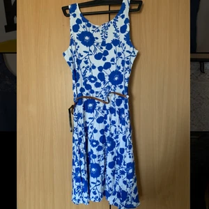 Sommar klänning vit/blå blommig  - Sommarklänning köpt i London. Vit med blåa blommor och ett brunt skärp. Skärpen är dock trasig, därav billigare pris. Jätteskönt material. Djupare urringning på baksidan. Har använts endast 1 gång. Kan skicka fler bilder vid förfrågan. Priset kan diskuteras. (Köp 3 plagg betala för 2) 