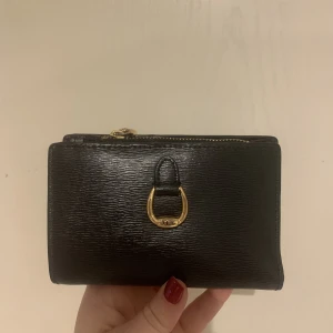 Ralph Lauren plånbok svart  - En svart äkta Ralph Lauren plånbok i svart. Detta är en lagom stor plånbok som rymmer både kontanter och kort, samt en ficka.  Köpt för cirka 1500, säljer för 500. 
