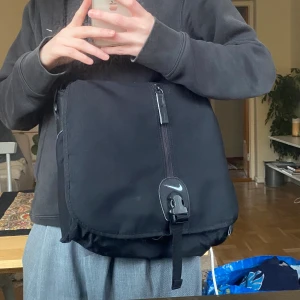 Nike väska - Svart axelremsväska från Nike. Sportig med många snygga detaljer, totalt fyra olika fack. Mångsidig storlek + justerbar rem. Bredd ca 38cm Höjd ca 33cm Djup cirka 20 cm.  Bruksslitage finns men inget som inte går att fixa själv! 