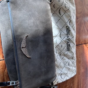 Zadig & Voltaire väska mocka  - Zadig Voltaire väska köptes på hemsidan för 3900 använd men i bra skick följer med dustabag och ett kortare band och ett längre band. Frakt tillkommer 