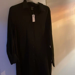 Lång klänning  - En svart lång klänning i nyskick, prislappen sitter kvar. sitter Super snyggt och om man vill lyxa till det lite kan man knyta t.ex ett bälte i midjan. Skönt tyg.