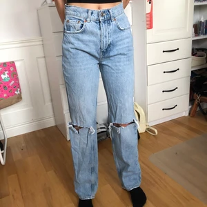 Blåa högmidjade jeans med hål - Storlek 34, passar i längden på en 168 cm person. Högmidjade med hål vid knäna. Byxorna passar till de mesta och har inspiration från 90-tal. Väldigt fina byxor som du såklart i garderoben din vill ha :)