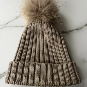 Mössa - En beige mössa med tofs av björnpäls. Tofsen är avtagbar om man skulle vilja tvätta mössan. I fint skick. 