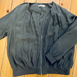 Sidenjacka gråblå - Äkta silke på utsidan och fodrad i acetat i liknande färg. Detta är en tunn innejacka som är snygg med linne, blus eller annan topp under.    Använd en gång.  Fraktpris tillkommer. 