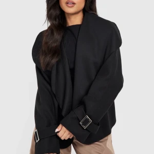 Dubbelbröstad kort kappa - Intressekoll på min extremt snygga svarta korta dubbelbröstade kappa. Har endast testat den hemma så den är verkligen helt ny. Slutsåld på hemsidan! (Modellen bär 36)