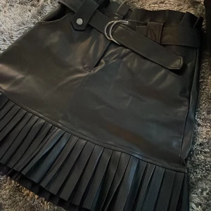 Svart Skinnkjol  - Svart kjol i fuskskinn med volanger och bälte i midjan💕 Mjukt sammet på insidan💕 För liten för mig, aldrig använd och i gott skick💕 Köpt på Zara, xs passar 34 eller mindre 36💕 Två fickor där fram
