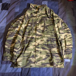 Militär jacka -  Kamouflage jacka/rock, många fickor, snöre 2 snören vid midjan o neråt för o spänna jackan för o få en annan passform mm. Dm vid frågor.