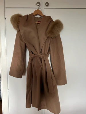 Max Mara Mango Coat Camel  - Fint skick och precis blivit kemtvättad och redo för användning. Material 100% ull. Storlek italiensk 38=svensk 34.  Avtagbar pälskant på huvan, fickor i sidsömmen, knapp ovanför bröstet & skärp i midjan.  Finns i Nacka, kan även skickas spårbart!