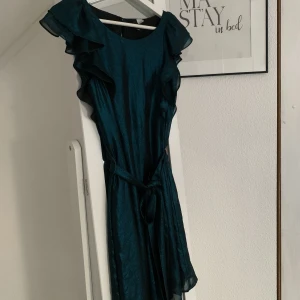 Glittrig klänning med volanger  - Supersöt glittrig grön/blå klänning med volanger på axeln/överkropp. Tyget är luftigt och väldigt bekvämt! 