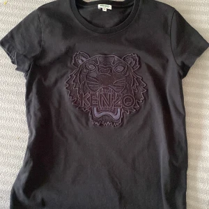 Helsvart Kenzo T-shirt  - T-shirt från Kenzo i boxig modell. Tröjan och märket är helsvart. Kraftig bomull i mycket bra kvalitet. Mycket gott skick, använd 1 gång, säljer pga lite för liten. Avklippt tvättetikett inne i tröjan pga skavde mot huden men självklart äkta Kenzo. 