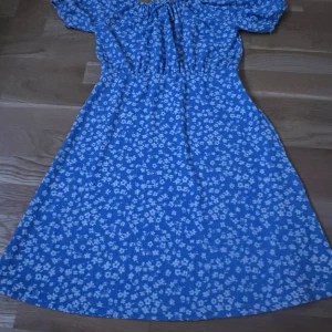 Klänning  - Säljer denna blåa klänning med vita blommor! Inga defekter. Hör av dig om du är intresserad! 