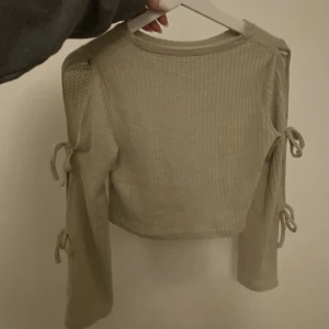 Beige / grön tröja - Beige grön tröja från shein. Aldrig använt, den har knytningar på ärmarna som man även kan låta vara öppna. Värde 100kr Säljer för 40kr