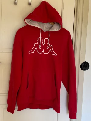 Röd hoodie  - Röd hoodie från Kappa. Använd ett flertal gånger och har en liten fläck på broderiet.