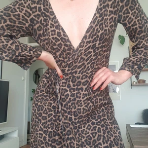 Leopardmönstrad omlottklänning  - Midklänning i tunnt material och markerad midja. Långa ärmar och knytning i midjan. Använd ett fåtal gånger och i gott skick. Även supersnygg öppen över en svart miniklänning eller lowrise jeans och vit topp 