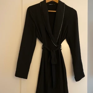 Svart klänning 34 - Svart klänning med band som knyts i midjan och silverdetaljer på kragen. Passar bra på fest! Storlek 34 men är mer som en 36-38 skulle jag säga. Bra skick.