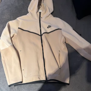 Nike tech beige storlek S - Säljer min Nike tech köpt från Nike för ett år sen. Säljer den eftersom den inte kommer till användning och är i bra skick. Skador på repen på dragkedjorna men inte så farligt. Hela sättet för 1300kr eller hoodie för 850kr och byxorna för 450kr