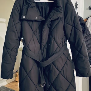 Varm vinterjacka från Vila  - Din, varm vinterjacka från Vila. Väldigt bekväm med ett spänne i midjan. På mig är jackan ner till knäskålarna jag är 161 cm.  Jag får enkelt plats på tjockare stickad tröja under. Eftersom det går att justera storleken med spännet är en tunn tröja bra. 