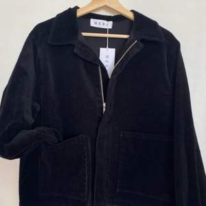 Unworn with label. Black corduroy jacket with front pockets. Zip front. Sleeves have poppers to close. Boxed shape. 