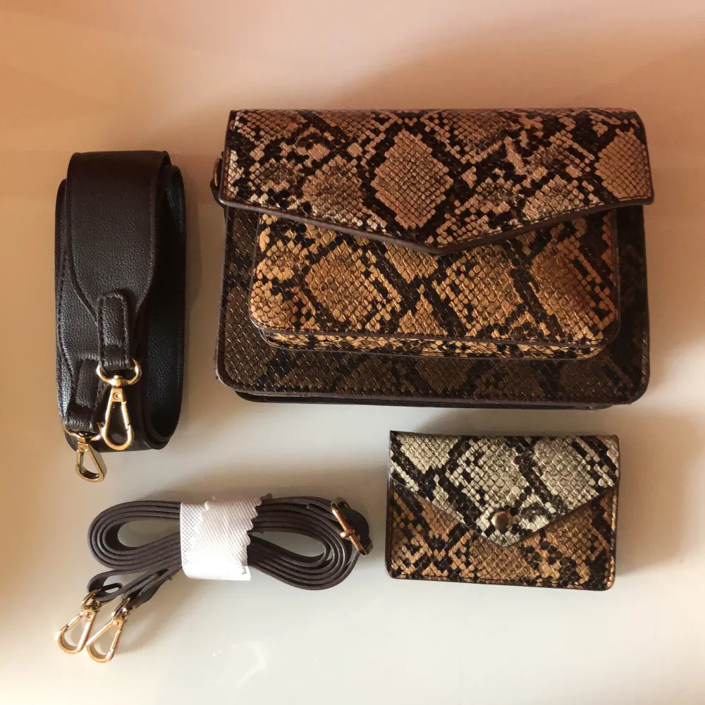 Väska med ormskinsmönster, matchande korthållare och två medföljande band i olika bredd.   Väskan är ca. 20x14 cm.. Väskor.
