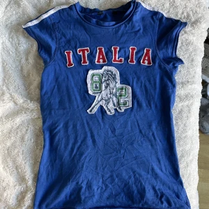 italia baby tee - snyggaste baby tee till sommar!! passar perfekt till lågmidjade jeans eller kjol, möter precis där low rise brukar börja. coolt och unikt plagg som ger lite 90-tals, y2k vibe!! lappen är borta men märket var Kikiriki. passar nog en 36/38 bäst!!