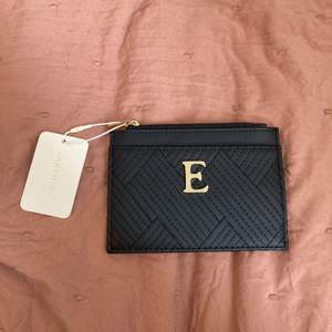 Oanvänd plånbok med ett guldigt E på sig.