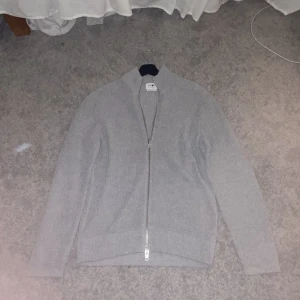 Cardigan full Zip NNO7  -  För fler bilder tveka ej på att höra av dig  Säljer min ljus grå cardigan ifrån NNO7 som är helt oanvänd pågrund av att jag tröttnat på den. För frågor och fler bilder tveka inte och höra av dkg 