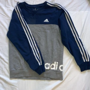 Adidastrjöja - Adidas tröja, knappt använd. Storlek M, unisex. Mörkblå och grå. Fin till både promenad, vardag och mys. Har en liten fläck på insidan, men som inte syns. 