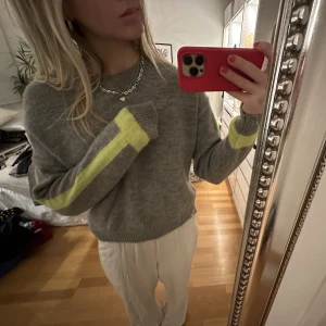 Stickad tröja med detaljer på ärmarna - Jättesnygg och skön grå stickad tröja med ränder på armarna i gul färg nästan lite neon. Strl S❤️