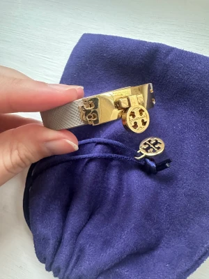 Tory Burch armband  - Armband från Tory Burch i grått läder med gulddetalj. Nyskick då det knappt kommit till användning. Tygpåsen smycket kom i medföljer.  