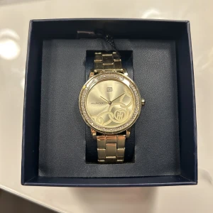 Tommy hilfiger guldklocka  - Klockan är köpt i december och den skulle ha lämnats tillbaka men hann inte. Den är helt orörd, plasten  finns kvar på klockan och plomberingen. 