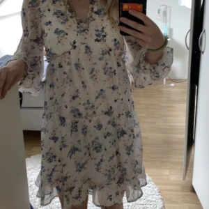 Klänning från Vero Moda - En blommig klänning från vero moda perfekt för sommaren. Den har långa ärmar som är tunna. Slutar strax ovanför knäna. Storlek XS. Blå och rosa blommar 