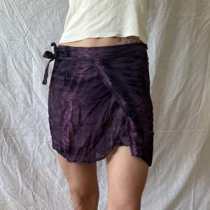Kort lila kjol med ormliknande mönster. Tunt tyg och band att knyta runt midjan. 