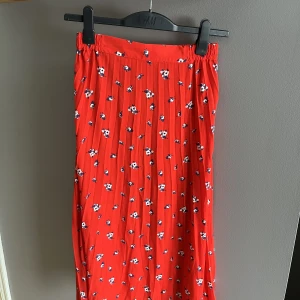 Plisserad kjol  - Fin plisserad kjol! Röda färgen med små blommor. Elastiskt midjeband, längd - 75-85cm (längre på sidorna). knappt använd, perfekt skick!