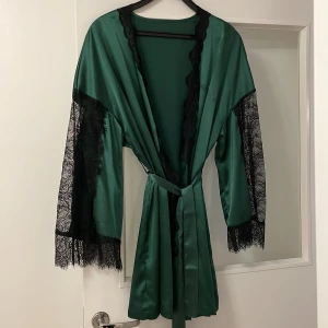 Mörkgrön rock - En mörkgrön rock i satin med spets i armarna. Stl L. I använd skick lite fläckar på ena sidan av bröstet.