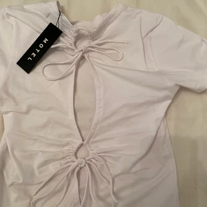 Vit t-shirt med fina rygg detaljer  - Jätte söt crop från Motel Rocks, helt ny med taggen fortfarande på. Säljer PGA att det inte är min stil. Passar jätte fint till sommar och är jätte skönt material. Fråga för fler bilder ❤️